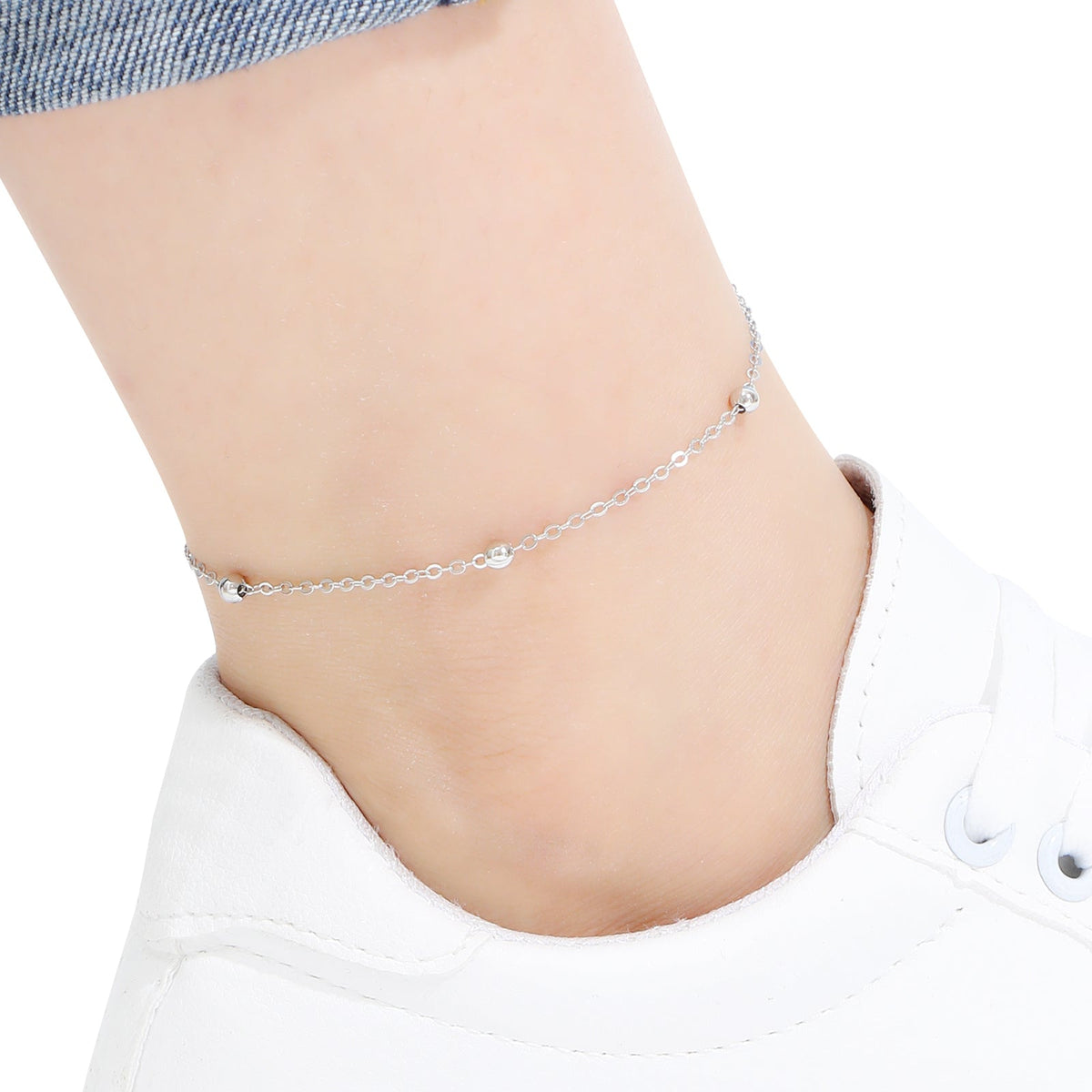 Silver beaded chain anklet on a person's ankle against a white background