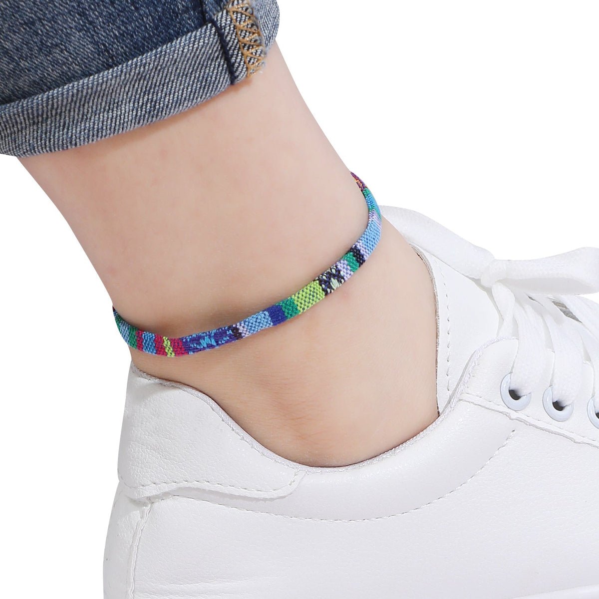 Colorful anklet on a person's ankle with a white sneaker and blue jeans.