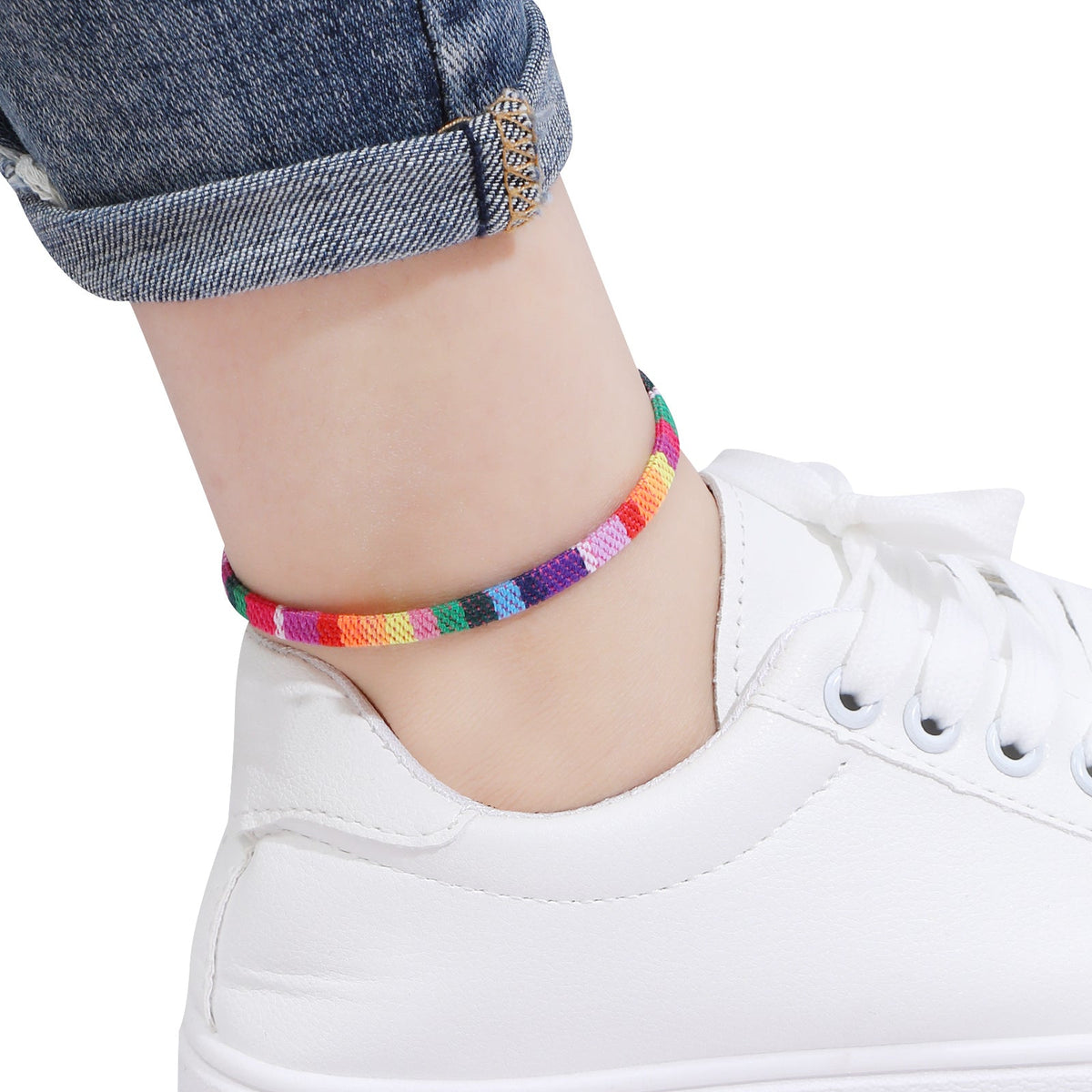 Colorful braided anklet on a person's ankle with white sneakers and rolled-up jeans.
