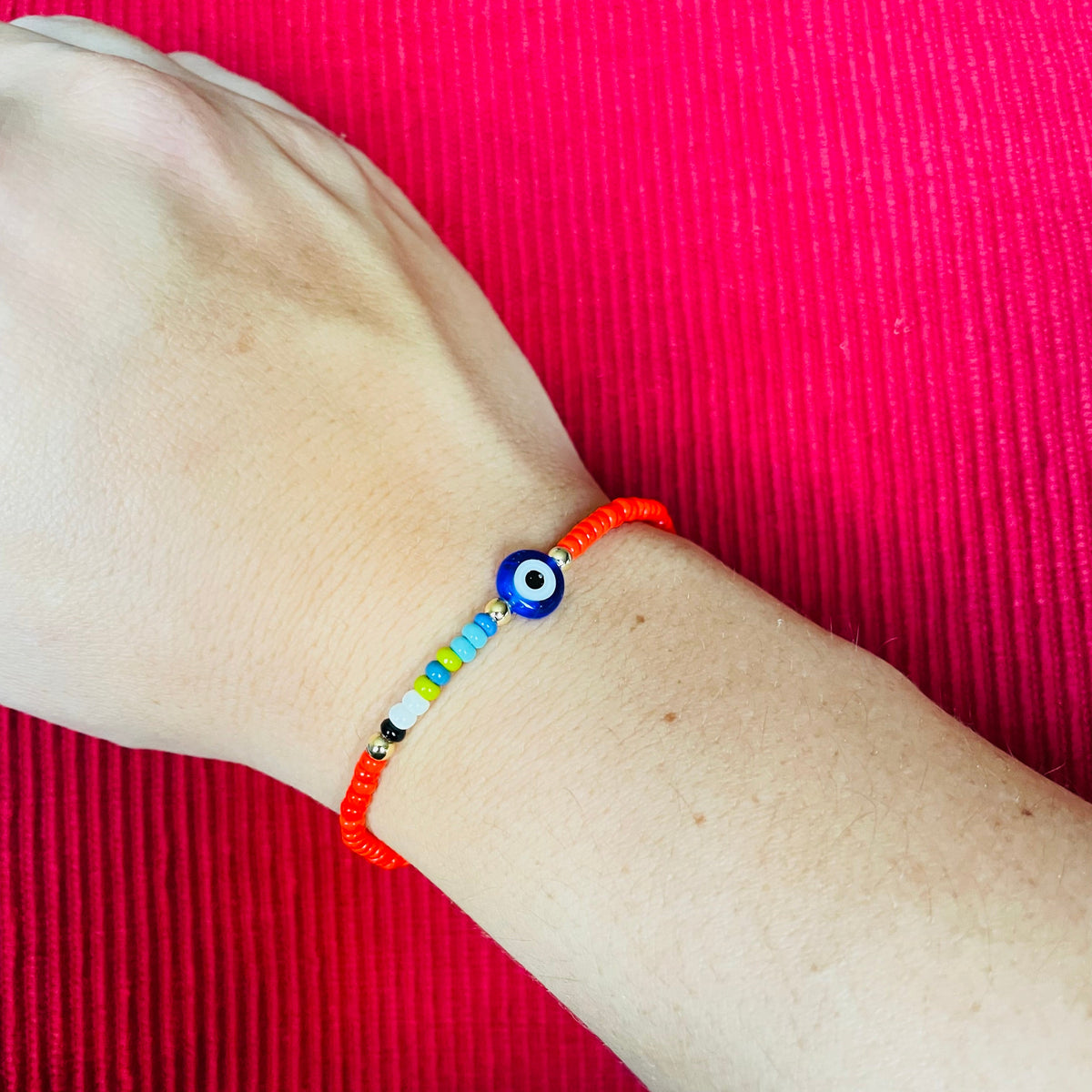 Colorful beaded bracelet with a blue eye charm on a wrist against a red fabric background