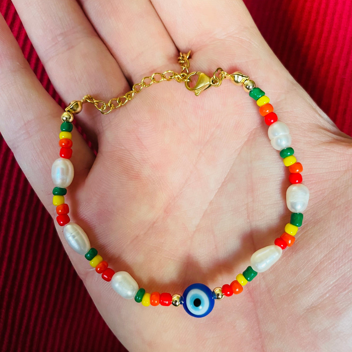 Colorful beaded bracelet with a gold clasp on a hand against a red background