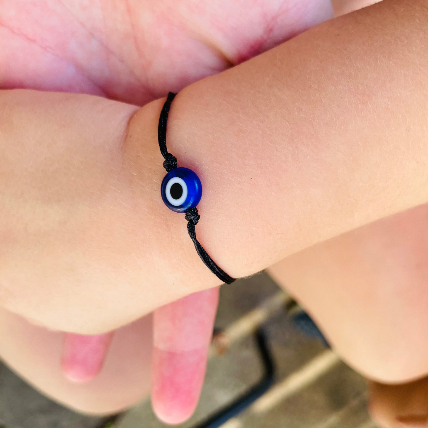 Close-up of a toddler wrist wearing a black string bracelet with blue evil bead