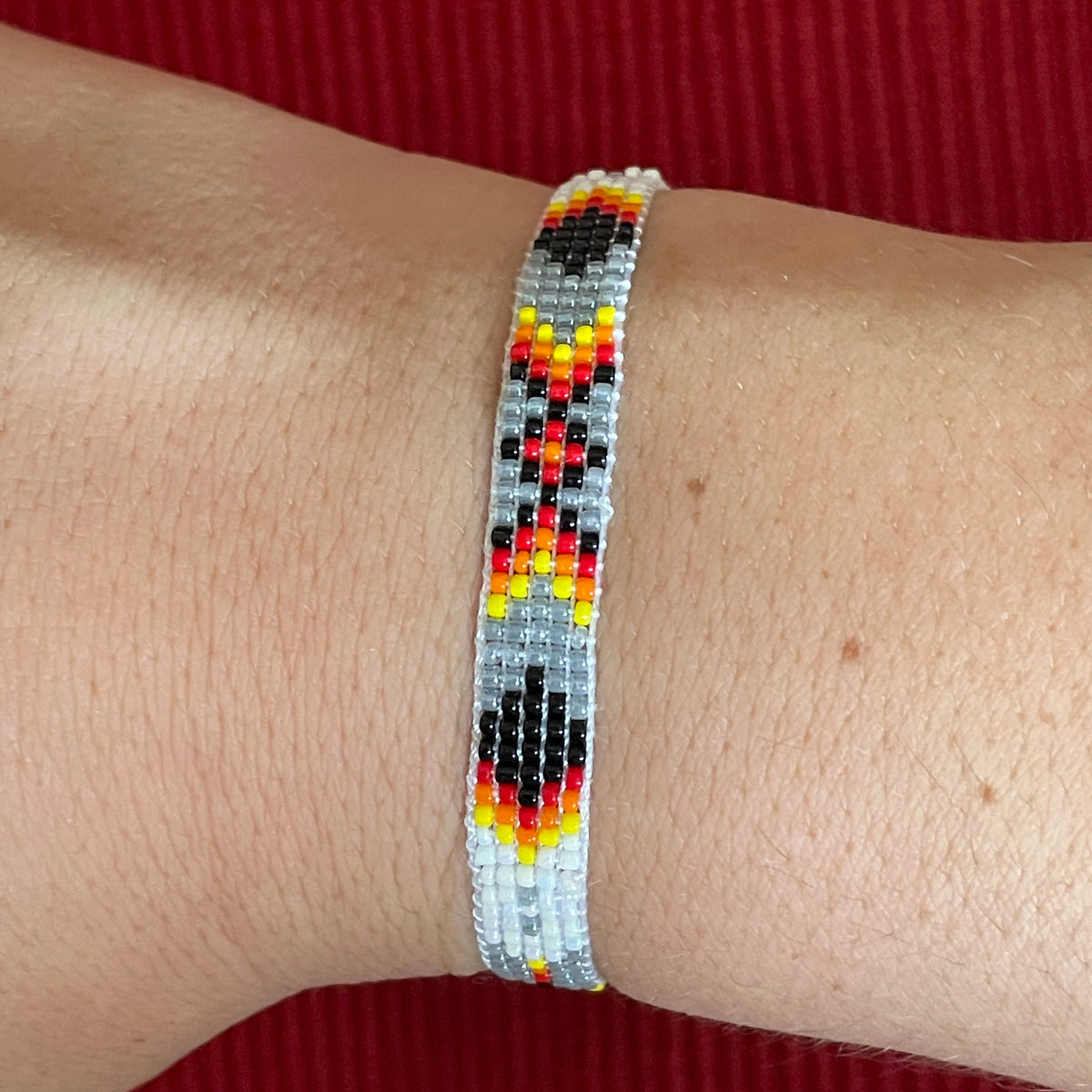 Beaded bracelet with red, yellow, and black pattern on a wrist against a red background