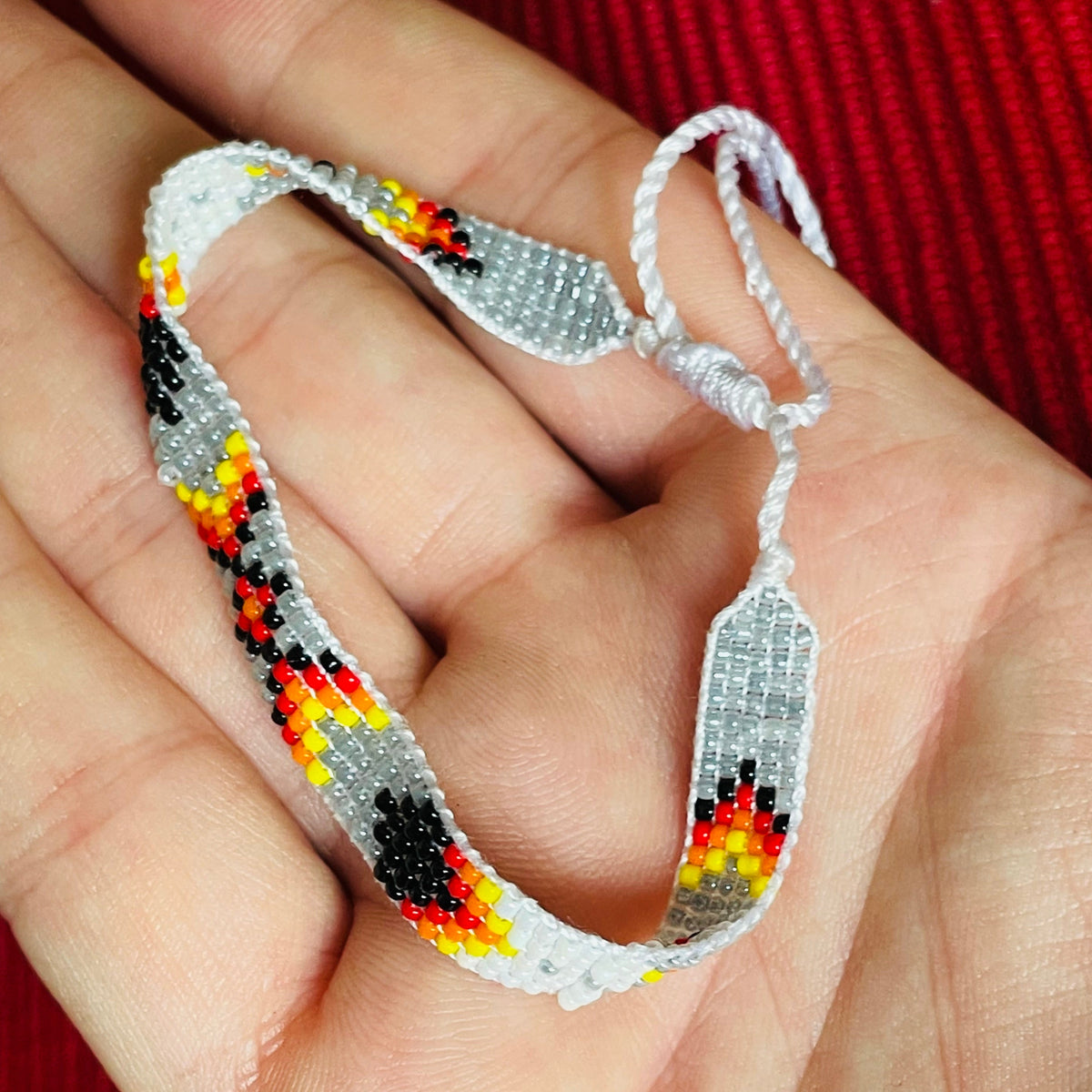 Hand holding a gray beaded miyuki woven bracelet with a sliding square knot with a red background