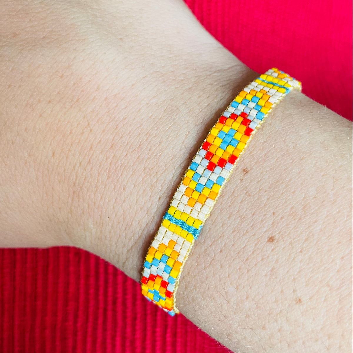 Yellow dominant colorful miyuki beaded bracelet on a wrist with a red background