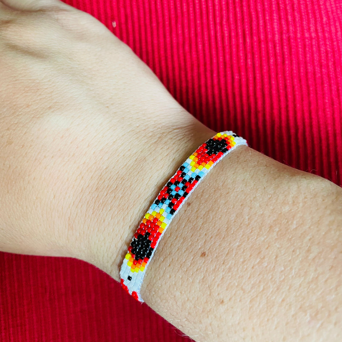 Close-up of a wrist wearing a colorful beaded miyuki bracelet against a red fabric background