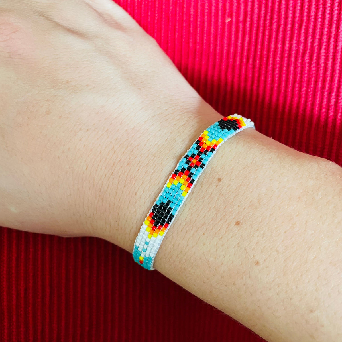 Multicolored beaded bracelet with turquoise, red, yellow, white and black beads a wrist against a red background