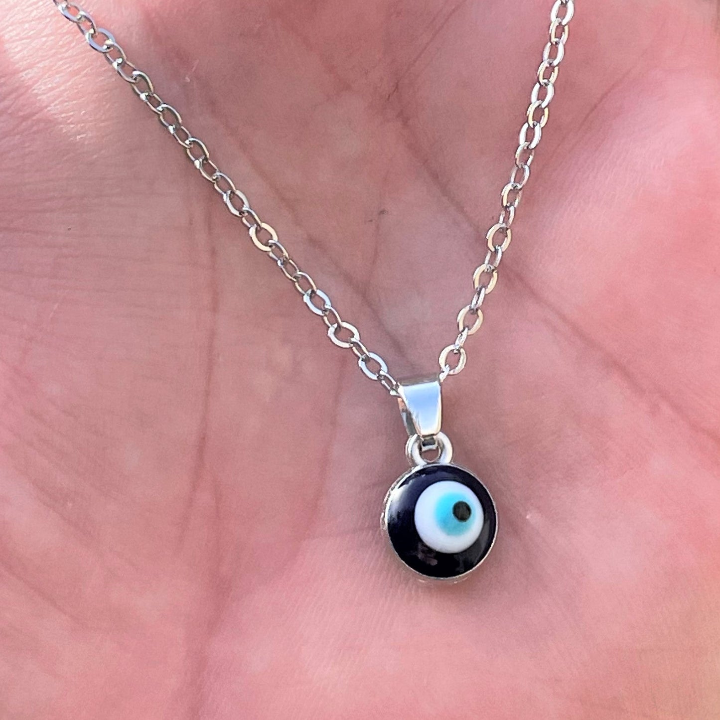 Hand holding a necklace with a tiny round eye pendant on a silver cable chain