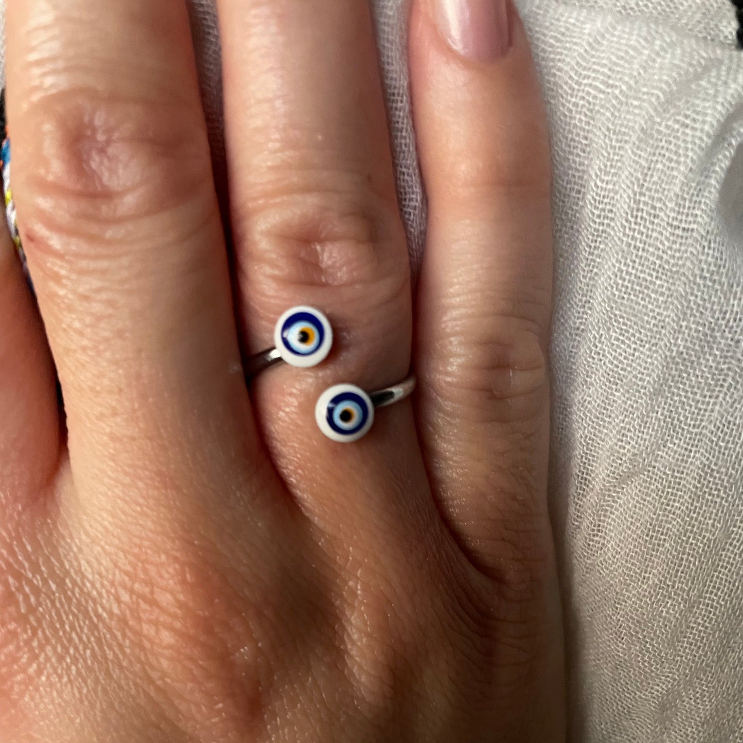 Close-up of a hand wearing a silver crossover wrap ring with a white eye design on a textured fabric background