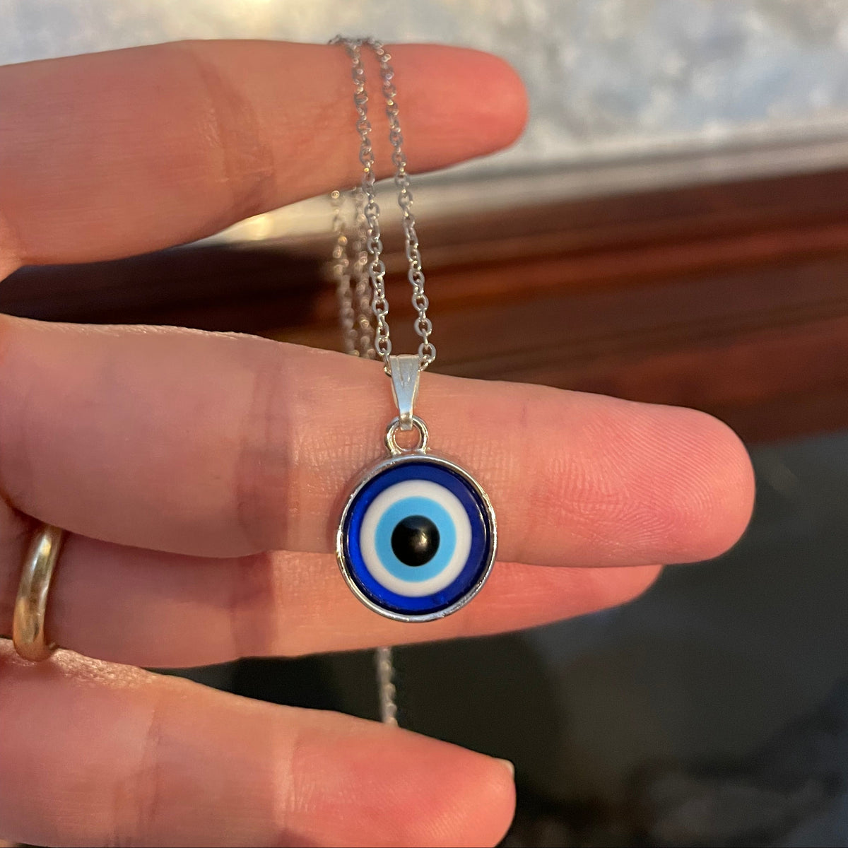 Hand holding a silver necklace with an evil eye pendant against a blurred background