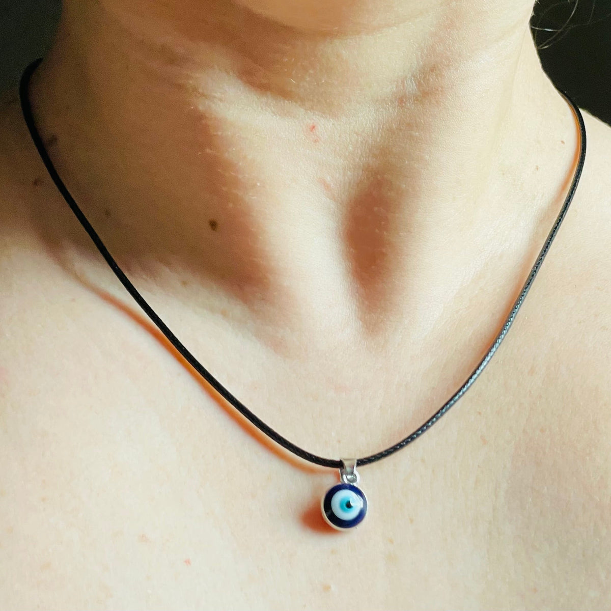Black cord chain with a small eye charm worn on a person's neck