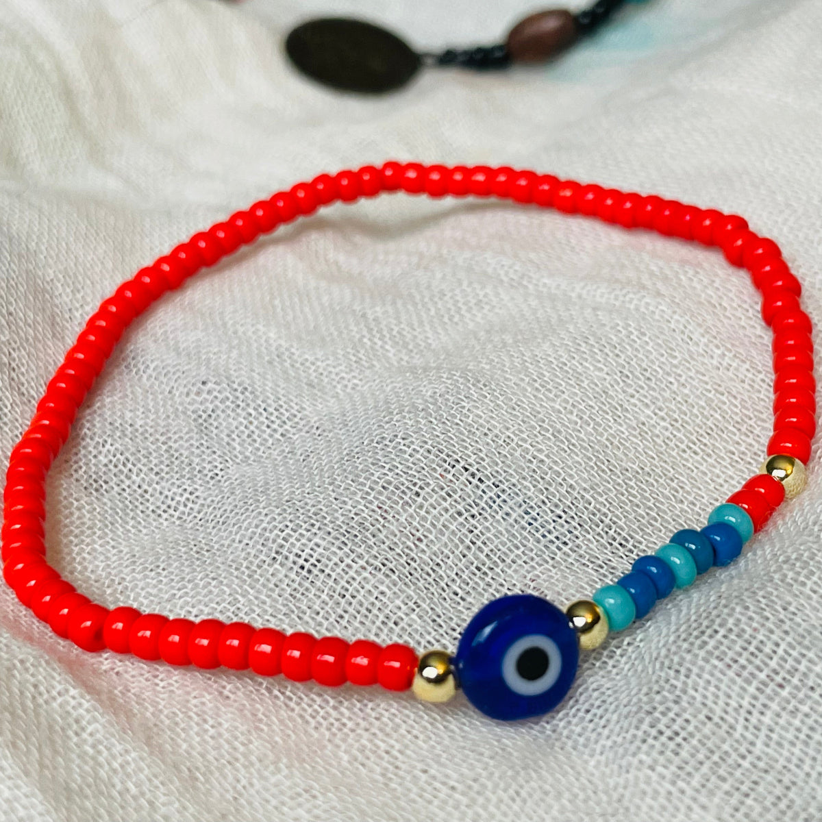 Beaded bracelet with a blue evil eye bead on a white fabric background