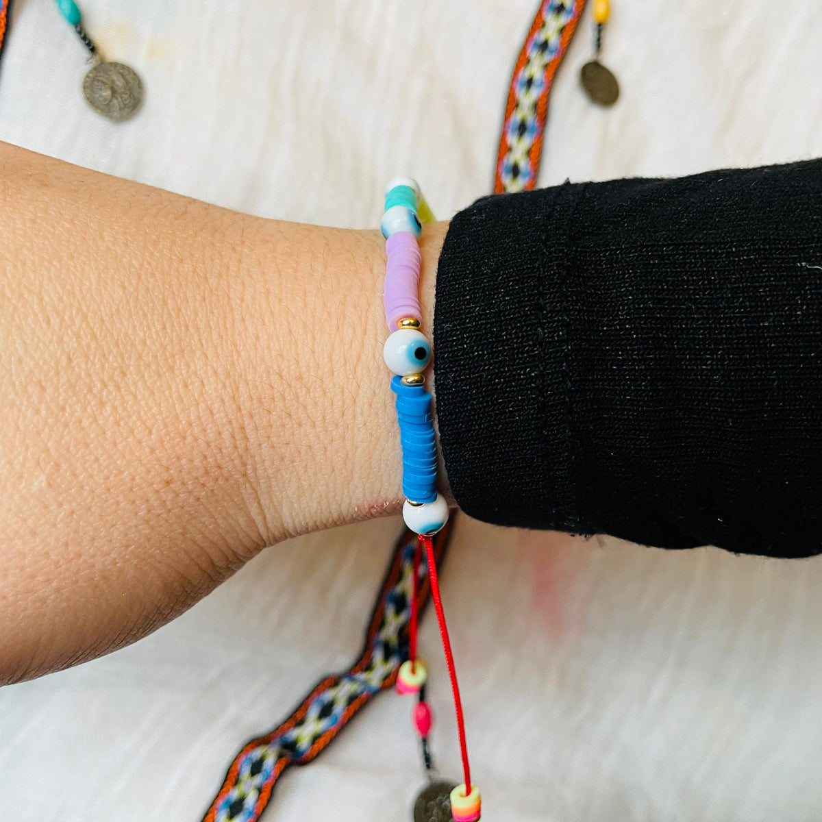 Side view of colorful beaded bracelet with a red string, on a wrist with a plain background