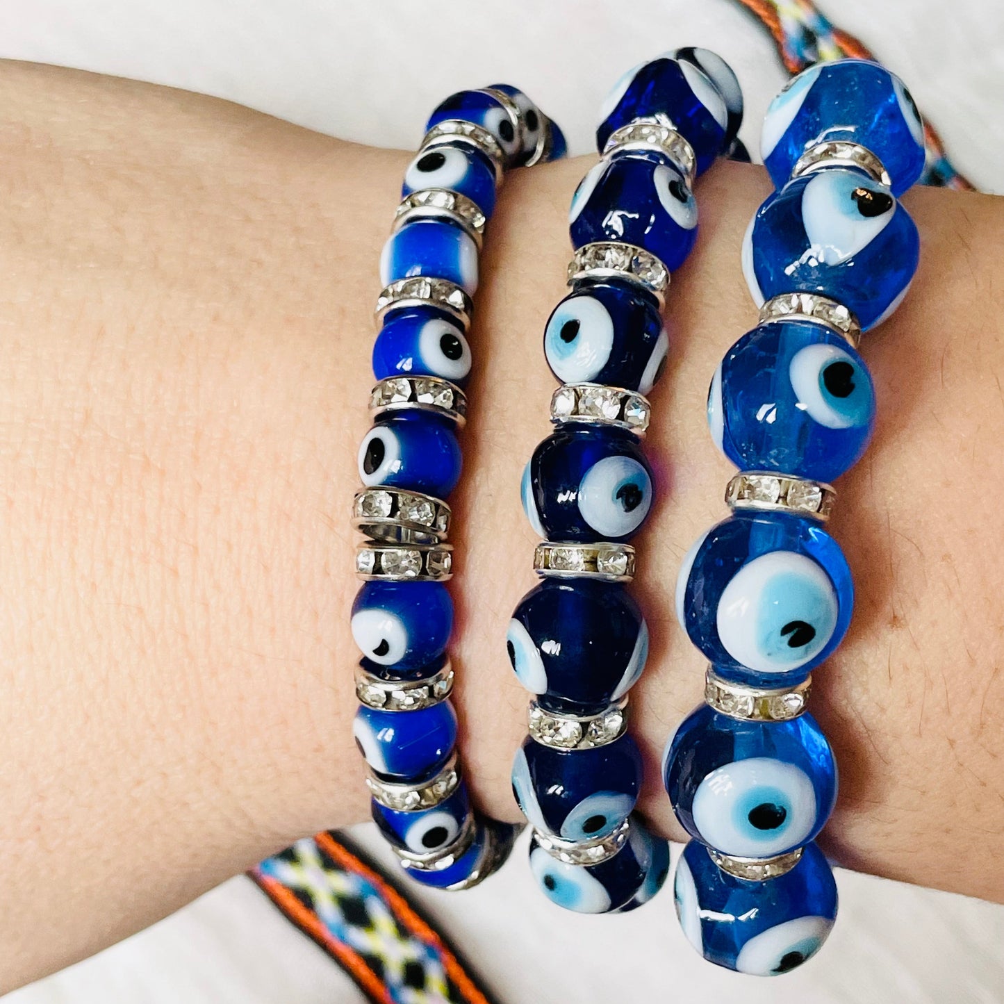 Close-up side view of blue glass eye bracelets with various bead sizes on a wrist with a white background