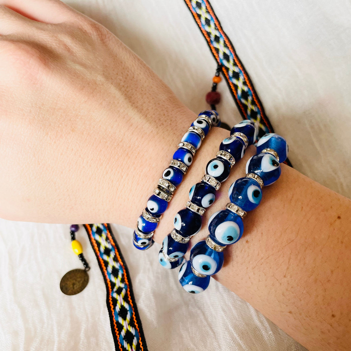 Wide angled view of hand wearing multiple blue evil eye bracelets on a white background