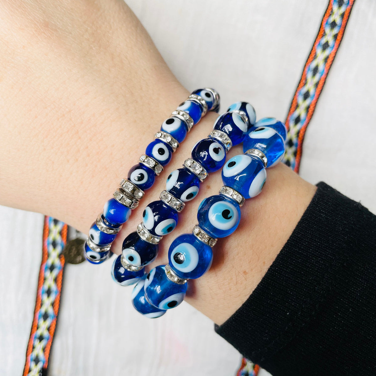Close-up of a wrist wearing three glass blue evil eye beaded bracelets on a white background.