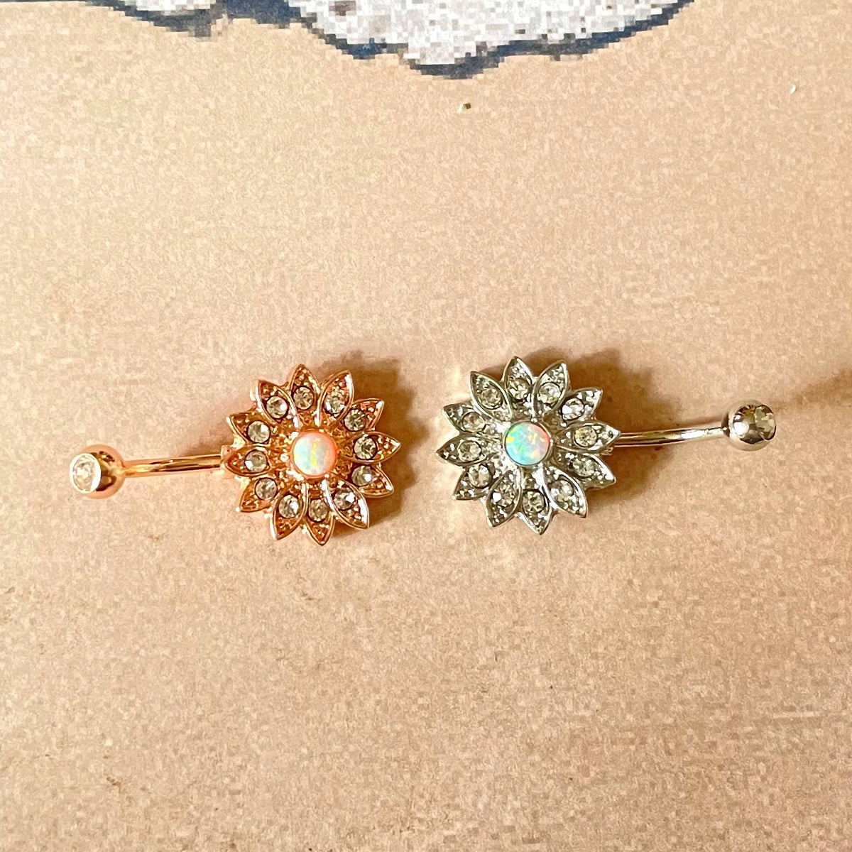 Two belly rings on sand with shells and a starfish, mimicking an ocean scene.