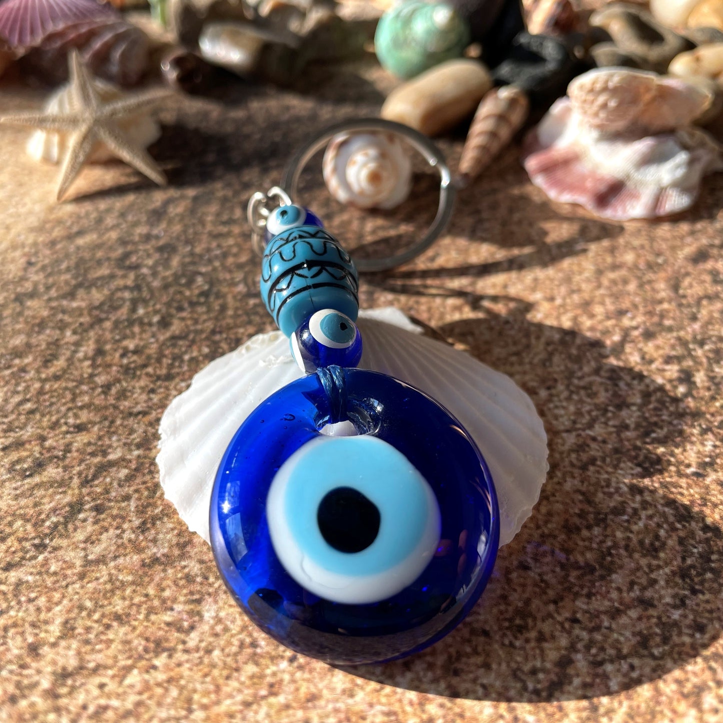 Blue evil eye keyring on a shell with seashells in the background