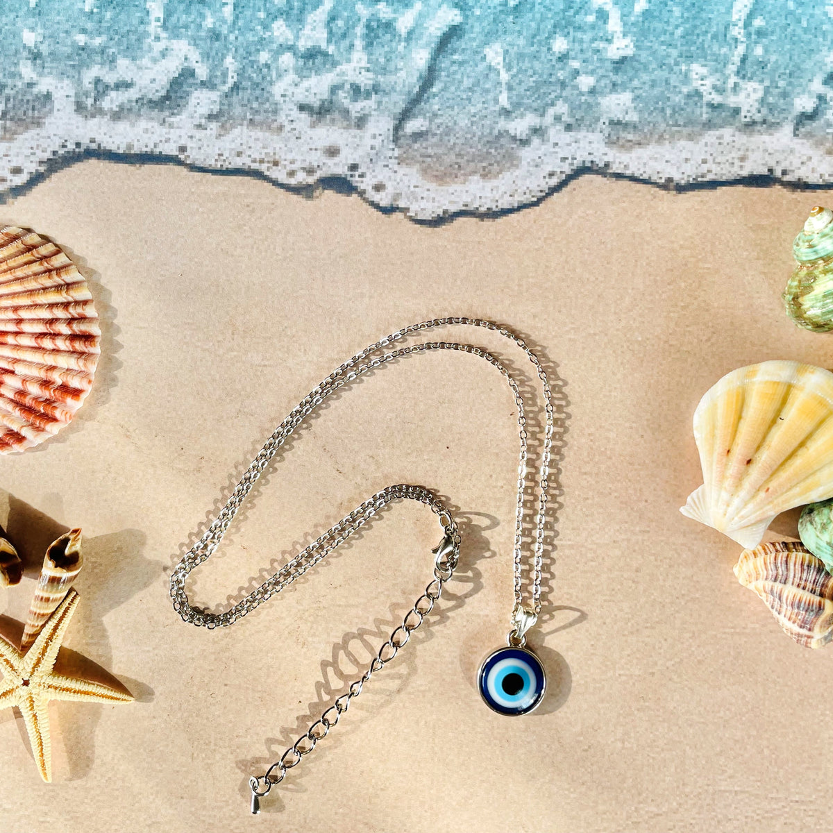 Necklace with an eye pendant on sand with shells and starfish, beach background