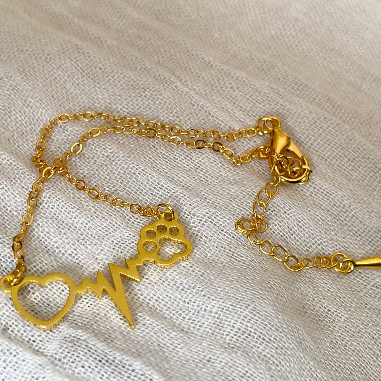 Gold bracelet with heart, paw, and heart beat charm on a light fabric background