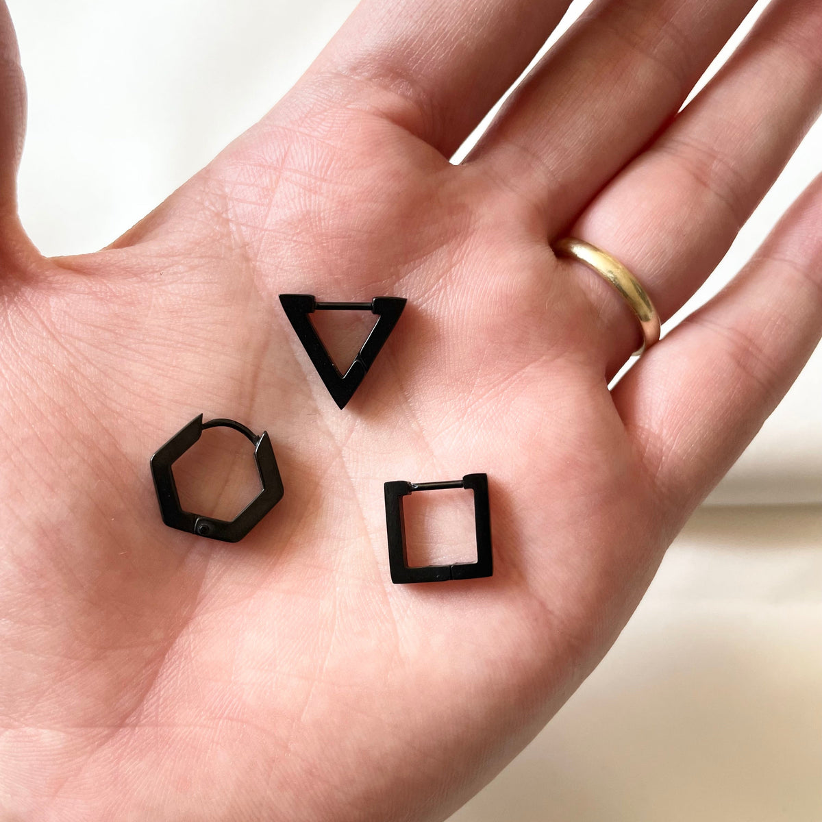 Three black geometric earrings on a hand with a plain background