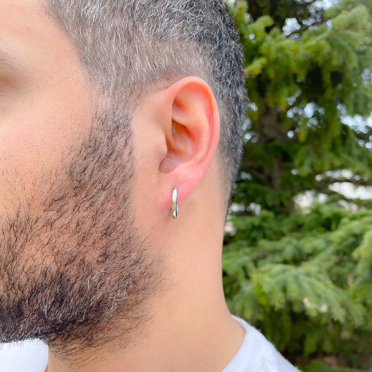 Close-up of a man wearing a small silver hoop earring with a blurred green background