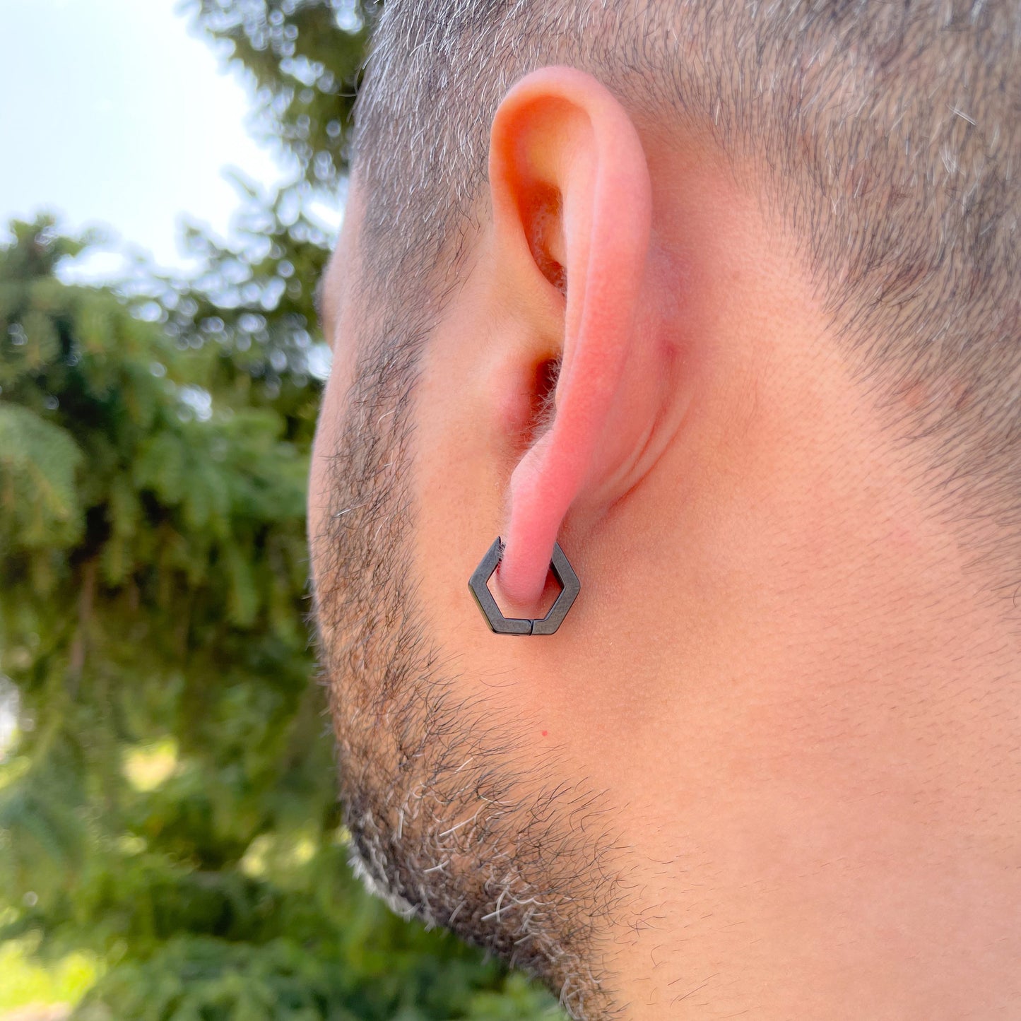 Close-up back view of a man wearing geometric hexagonal earring with a blurred green outdoor background