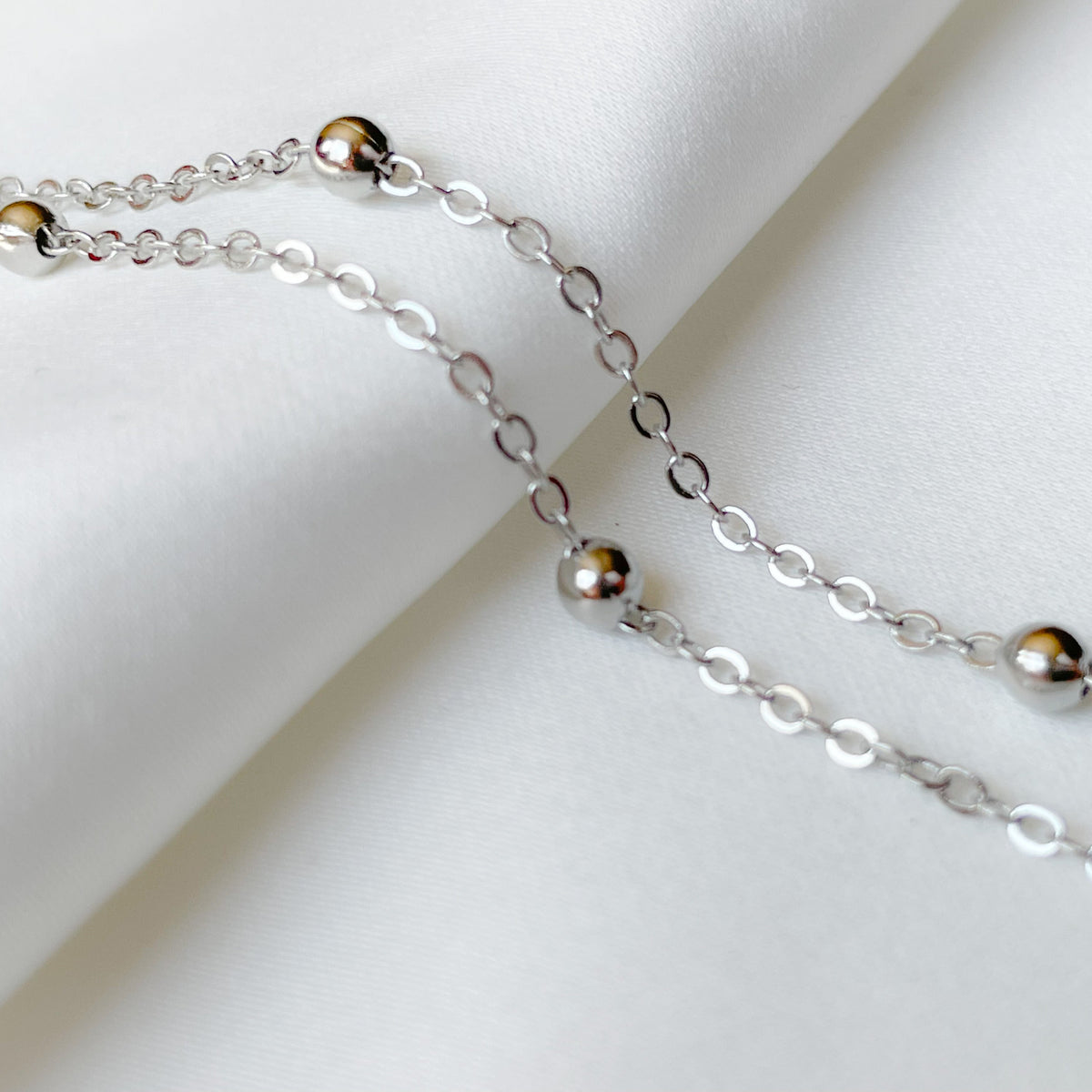 Close-up view of silver satellite chain anklet on a white background