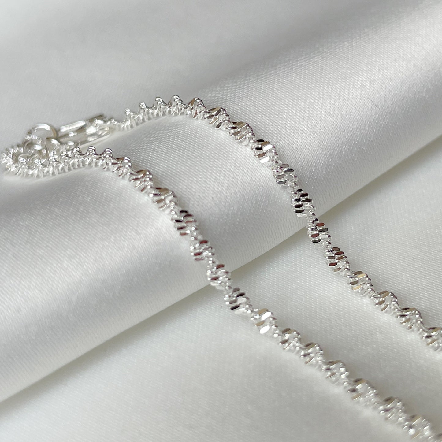 Close- up view of the dainty silver singapore chain on a white fabric background