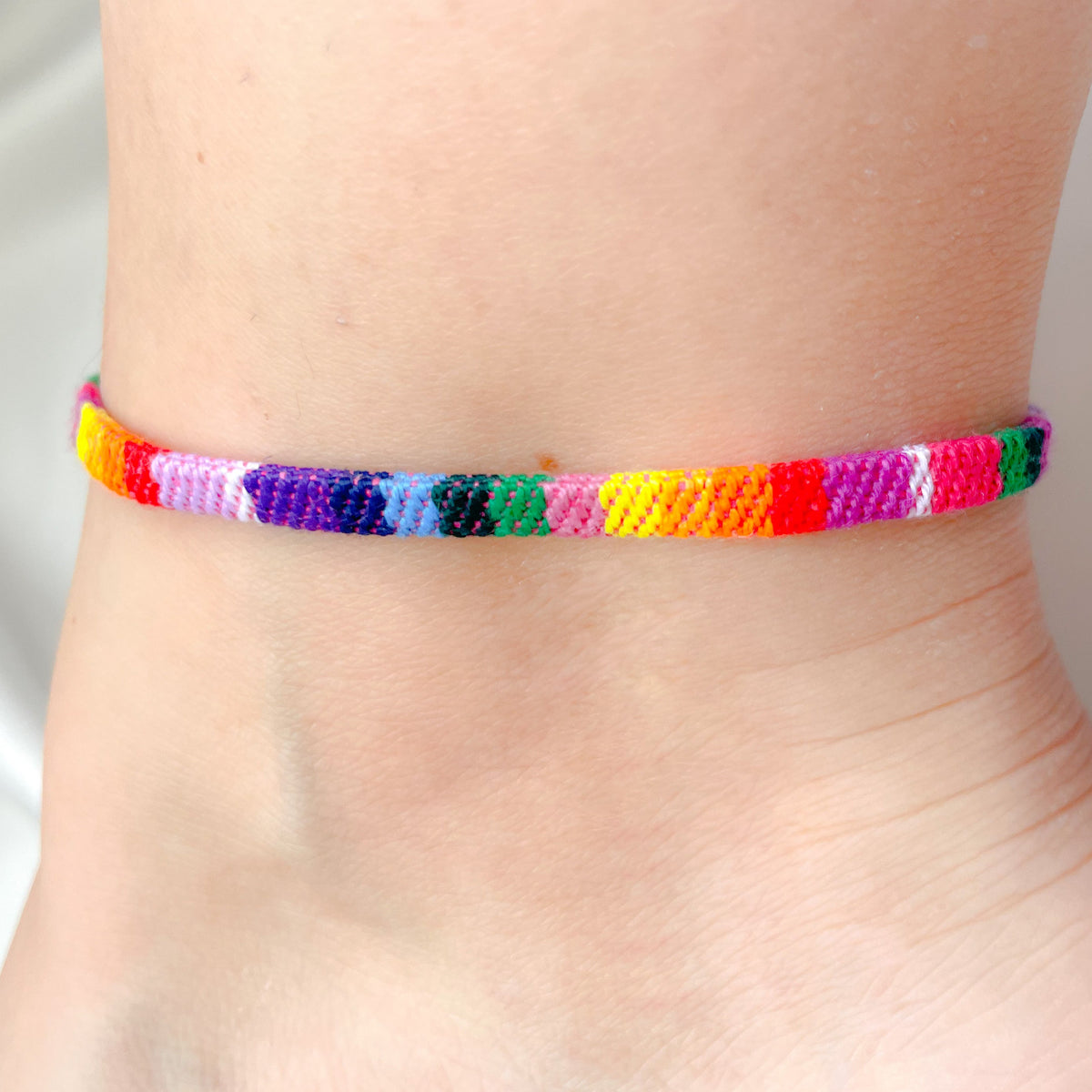 Colorful braided ankle bracelet on a person's ankle against a neutral background