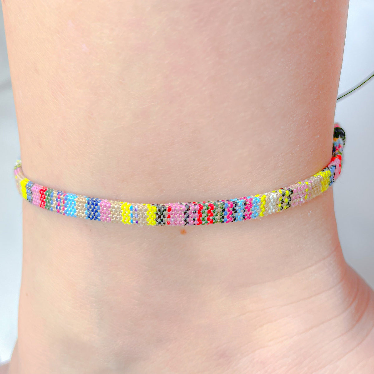 Yellow dominant colorful surfer friendship anklet on a person's ankle against a neutral background