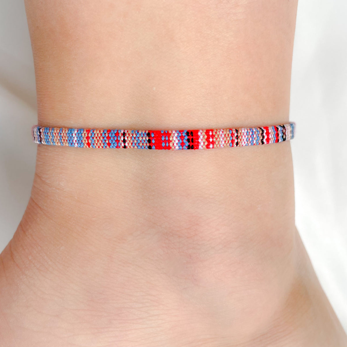 Red and blue dominant Multicolored braided boho anklet on a person's ankle against a white background