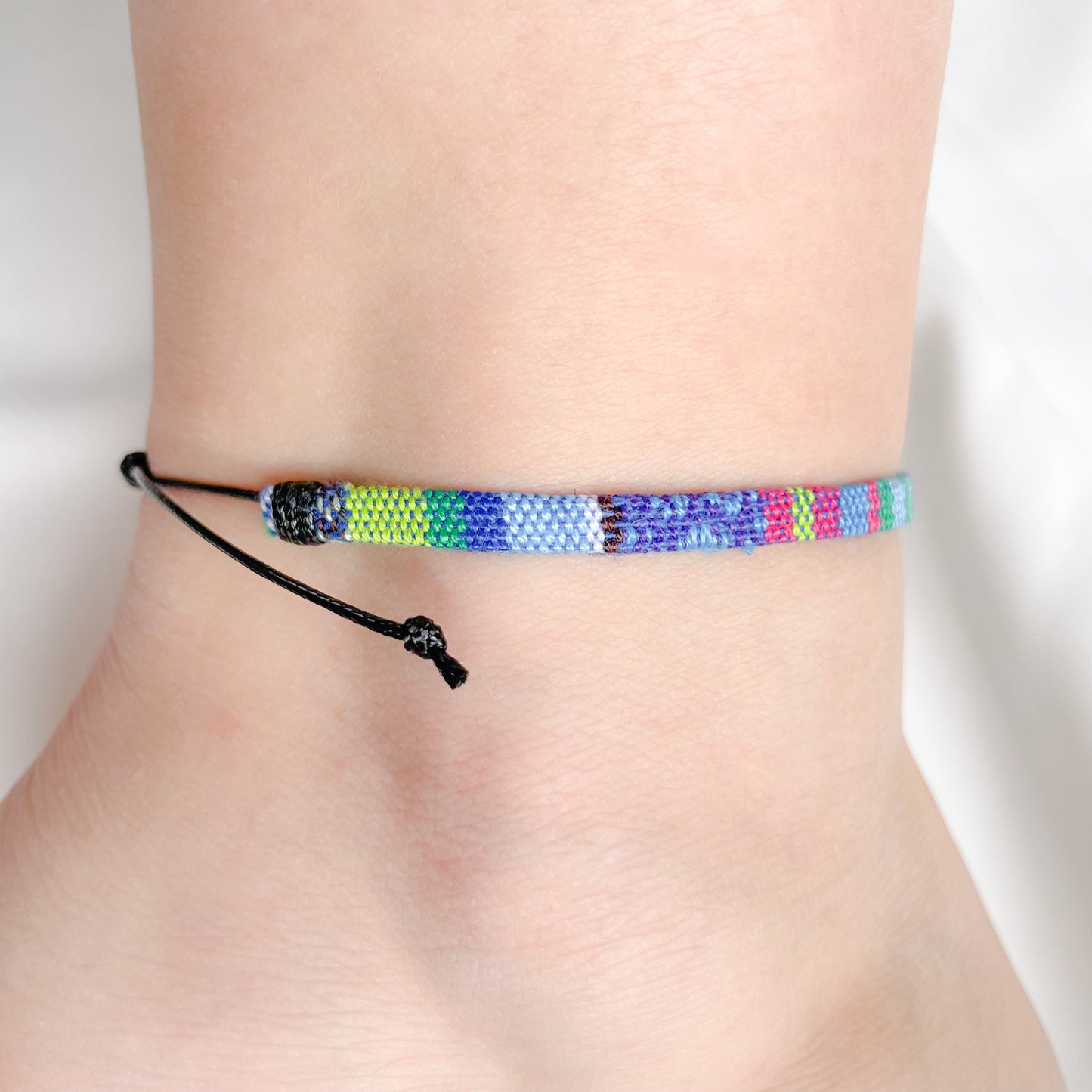 Blue and green dominant multicolored friendship anklet on a person's ankle against a white background