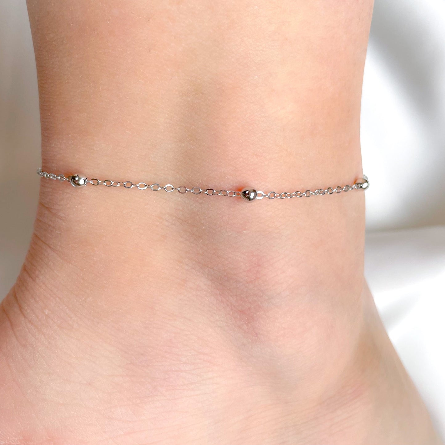 Silver ball chain anklet on a person's ankle against a neutral background