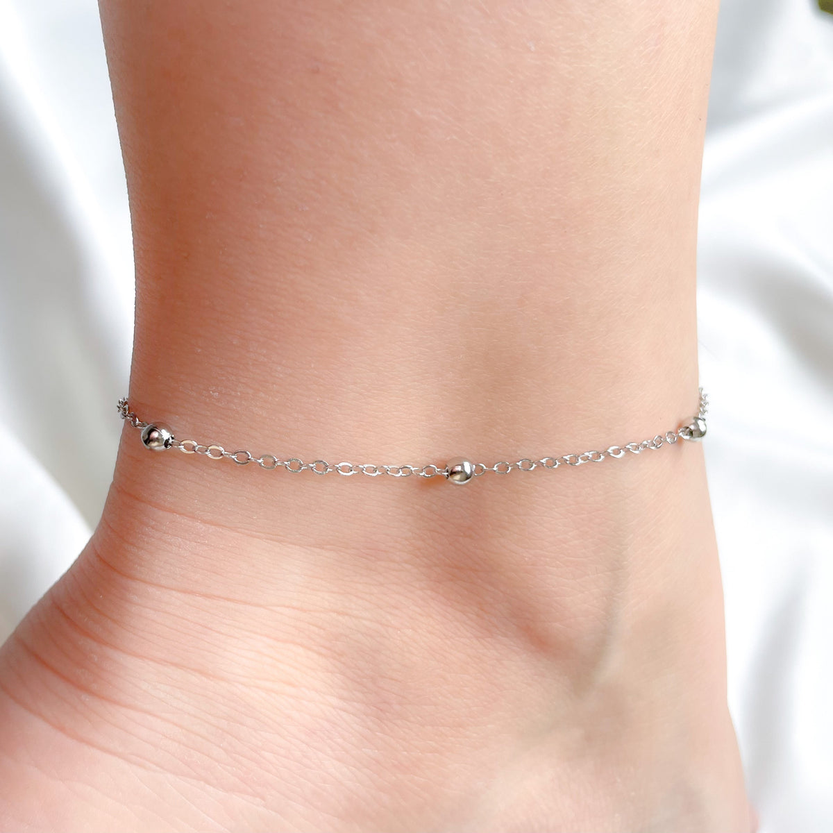 Dainty sterling silver ilver anklet on a person's ankle against a white background