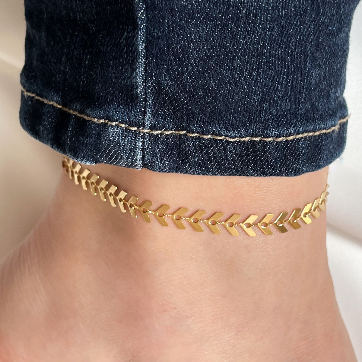 Thick gold anklet on a person's ankle with a blurred background