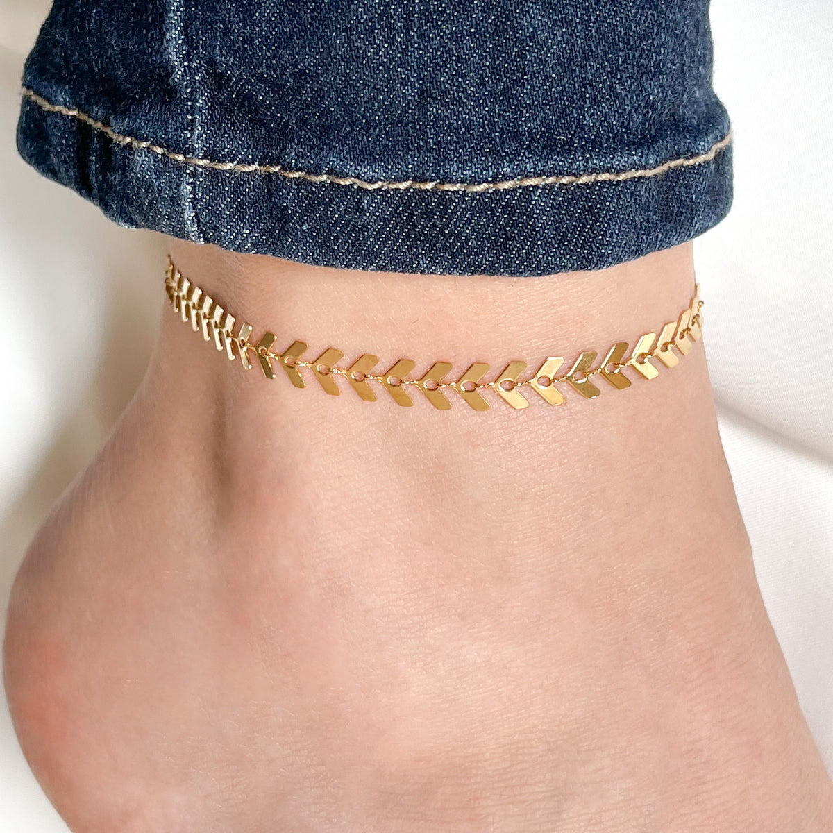 Front view of gold leaf chain anklet on a person's ankle with denim jeans