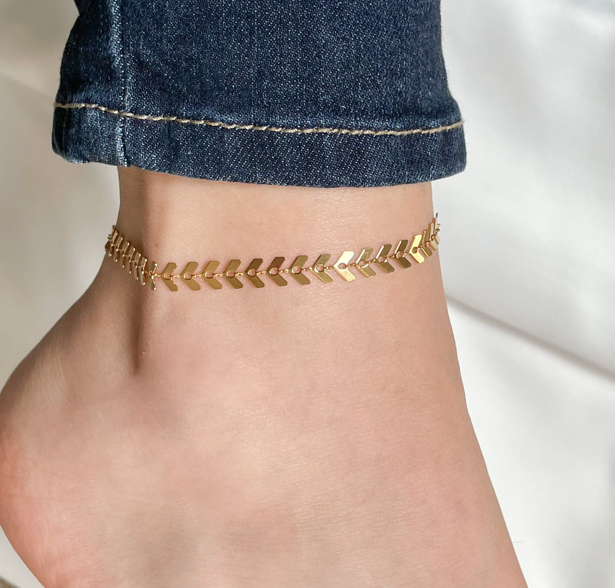 Gold chevron link anklet with high-polish finish worn on an ankle with denim
