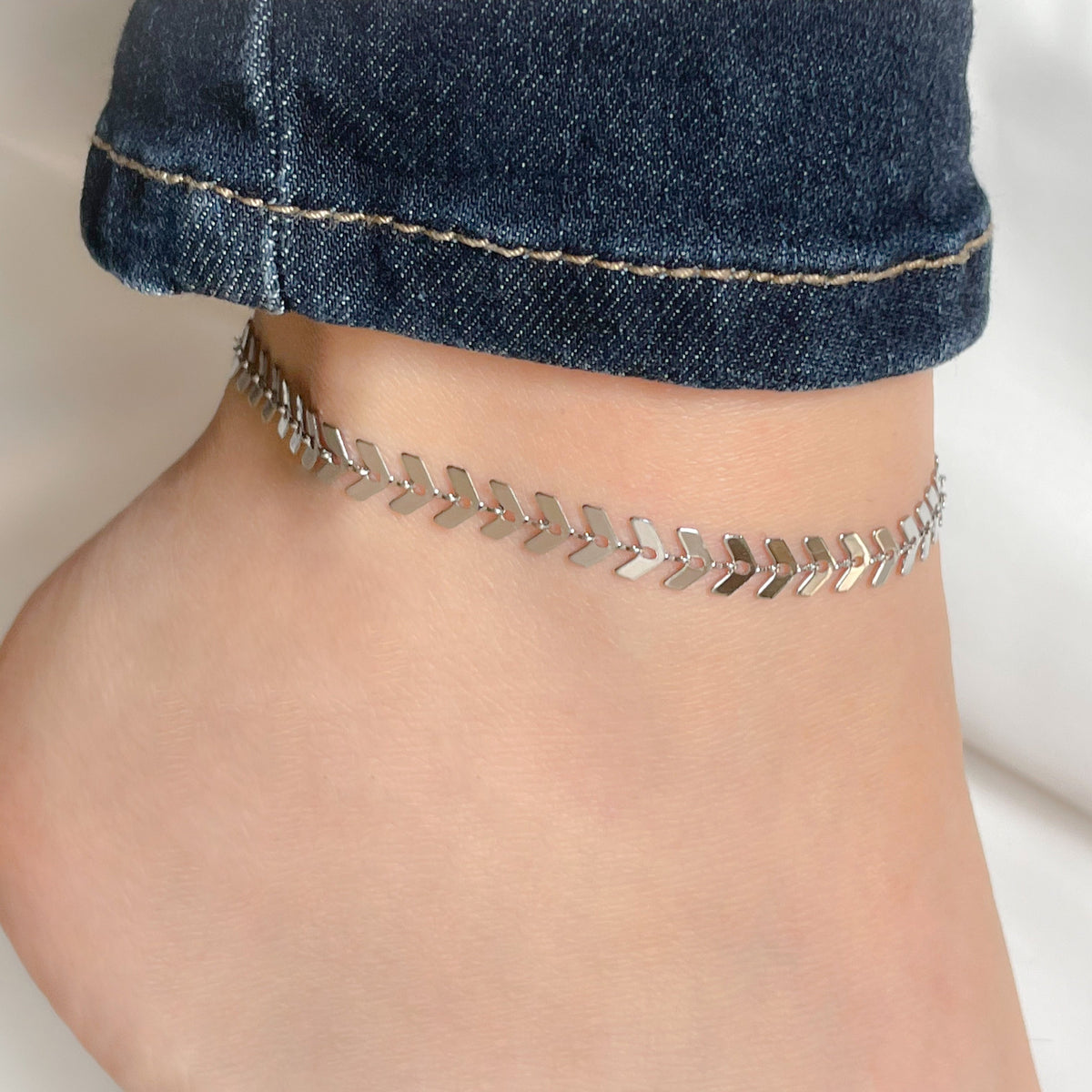 Geometric silver chain anklet worn on a person's ankle with a blurred background