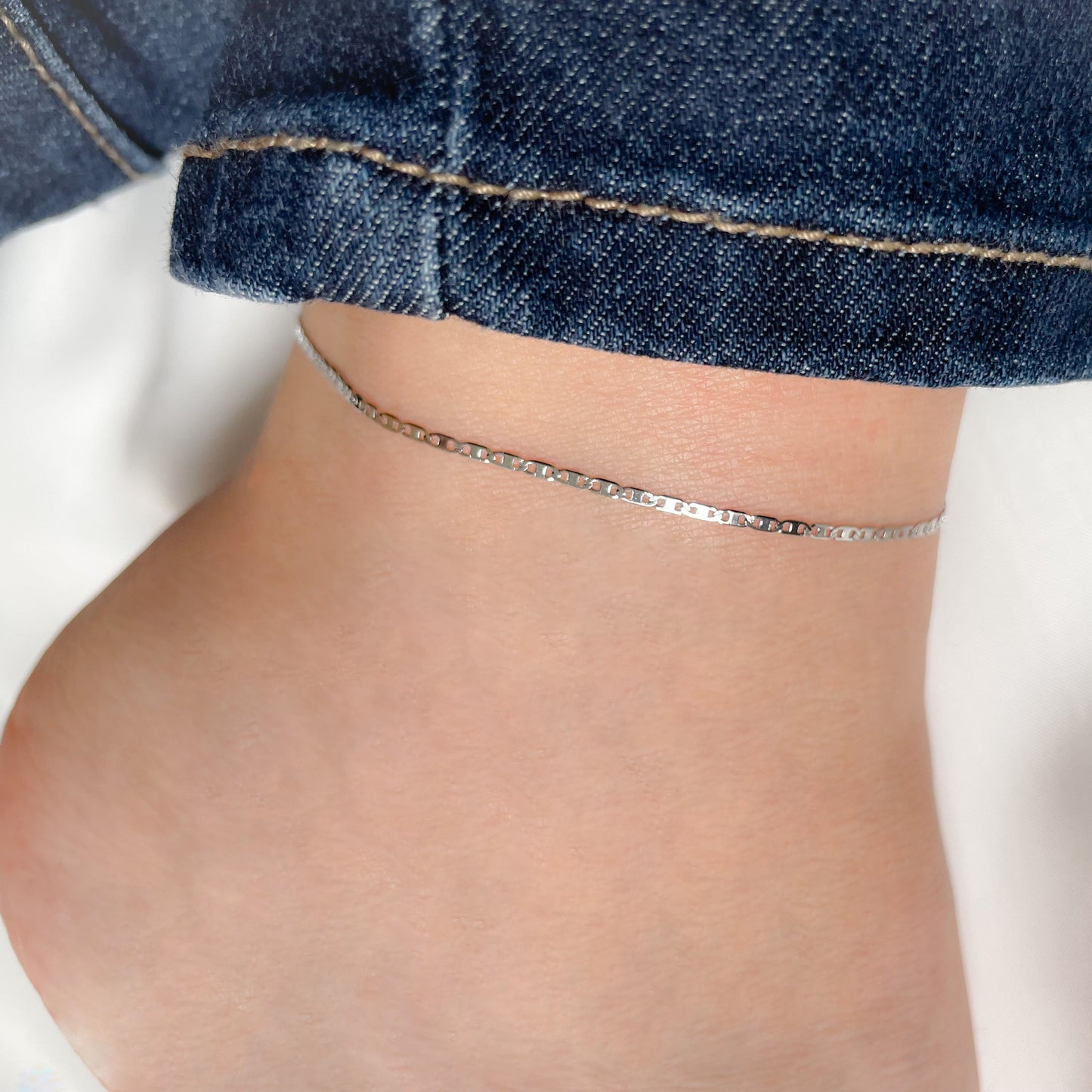 Silver anklet on a person's ankle with rolled-up jeans