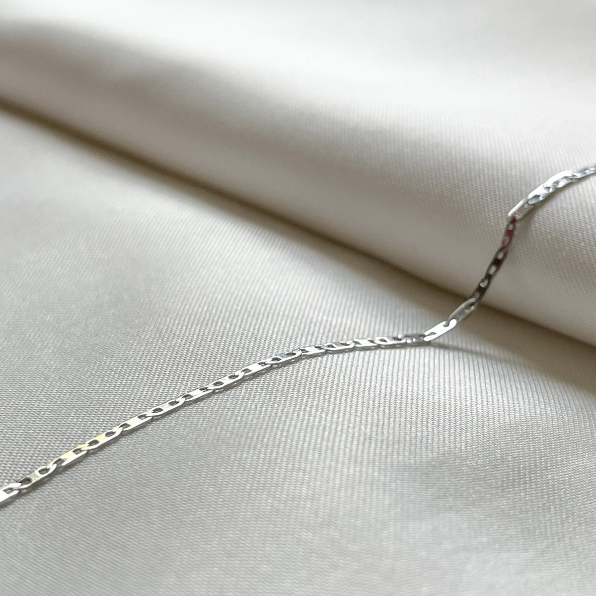 Thin silver mariner chain on a light fabric background