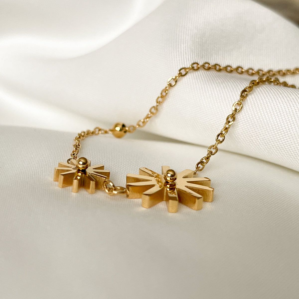 Gold anklet with a flower charm on a white fabric background