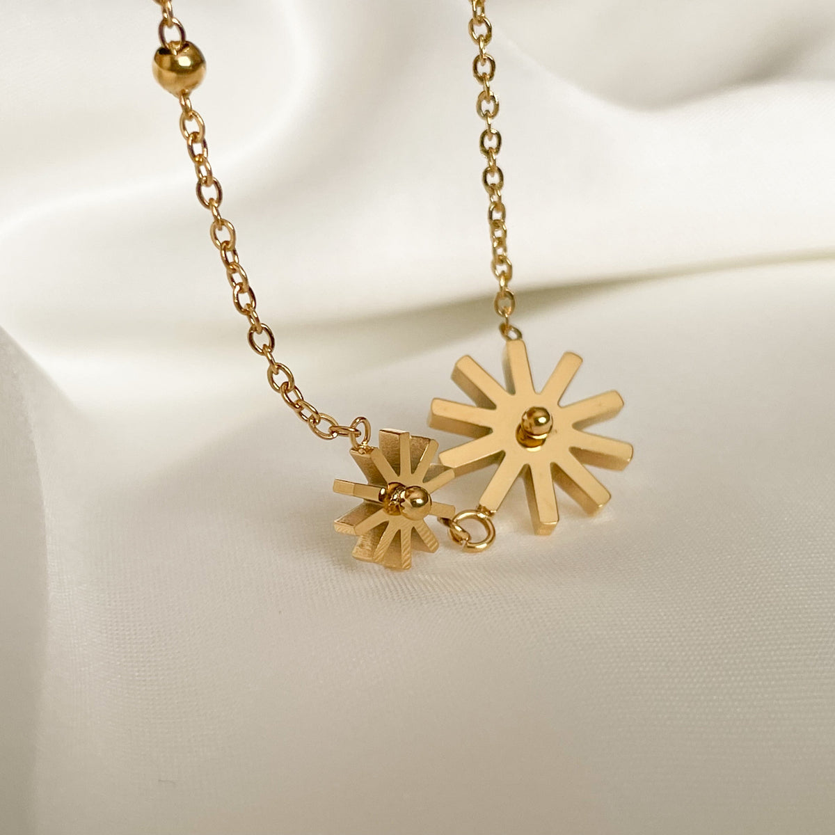 Gold anklet with one big and one small sunflower charms on a dlicate cable chain with a single gold bead accent on a white background