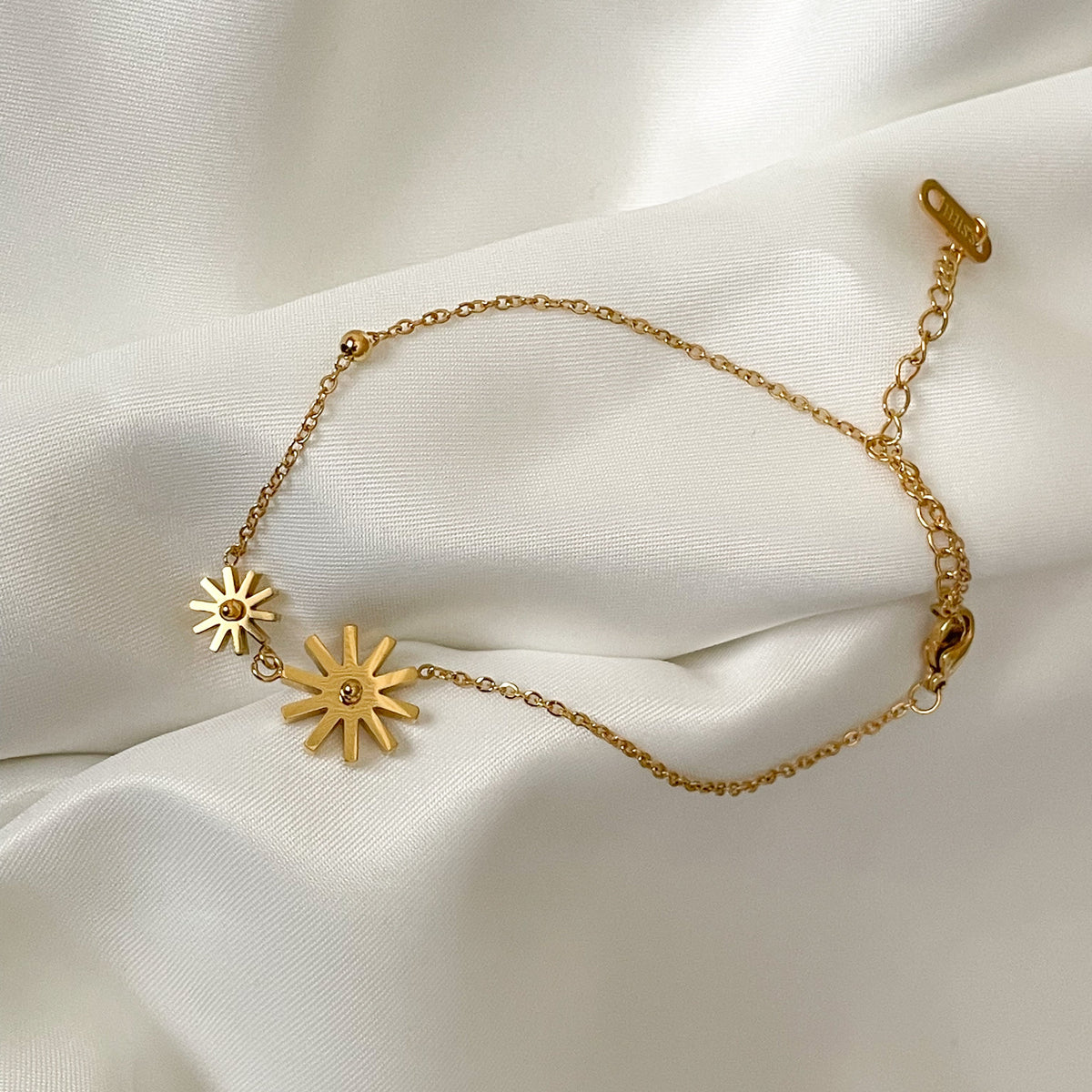 Gold ankle bracelet with star-shaped charms on a white fabric background