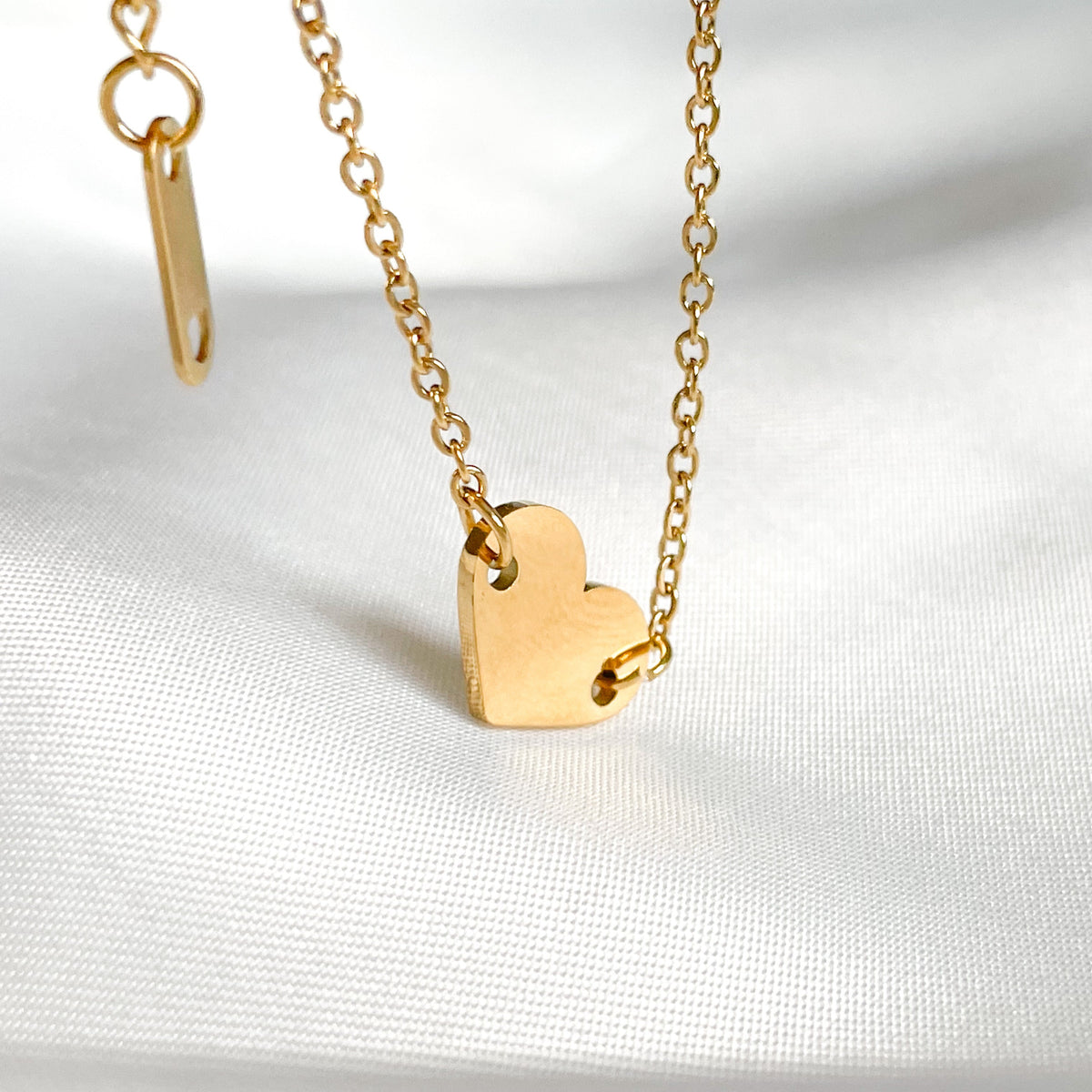 Front view of gold heart ankle bracelet on a white fabric background