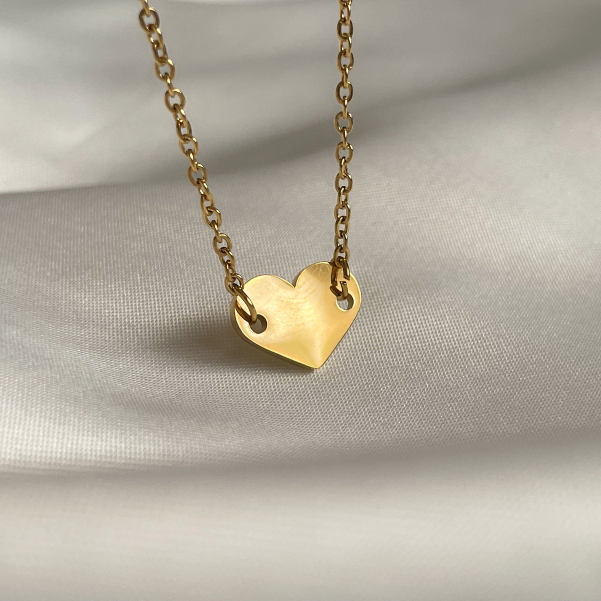 Gold heart charm anklet reflecting light on a soft gray background