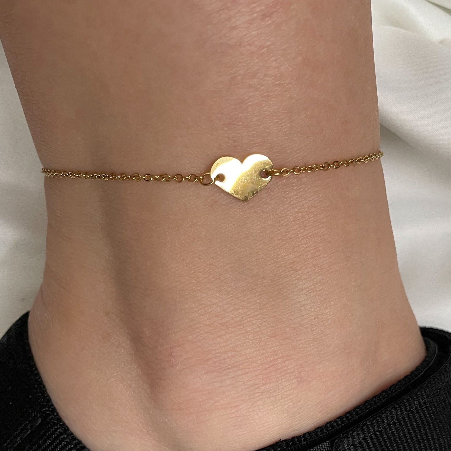 Gold anklet with a heart charm on a person's ankle against a white background