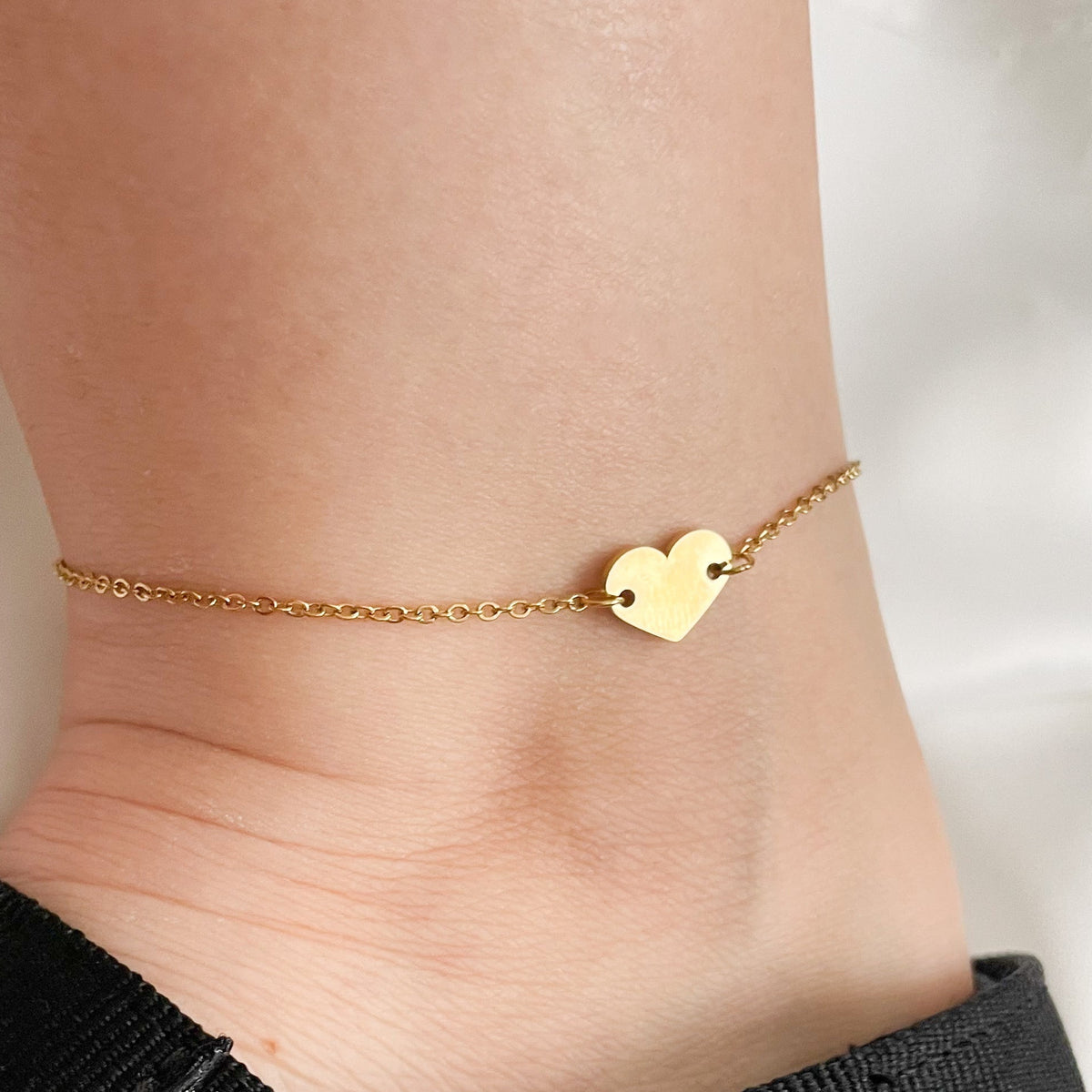 Gold heart anklet on an ankle with a black strap