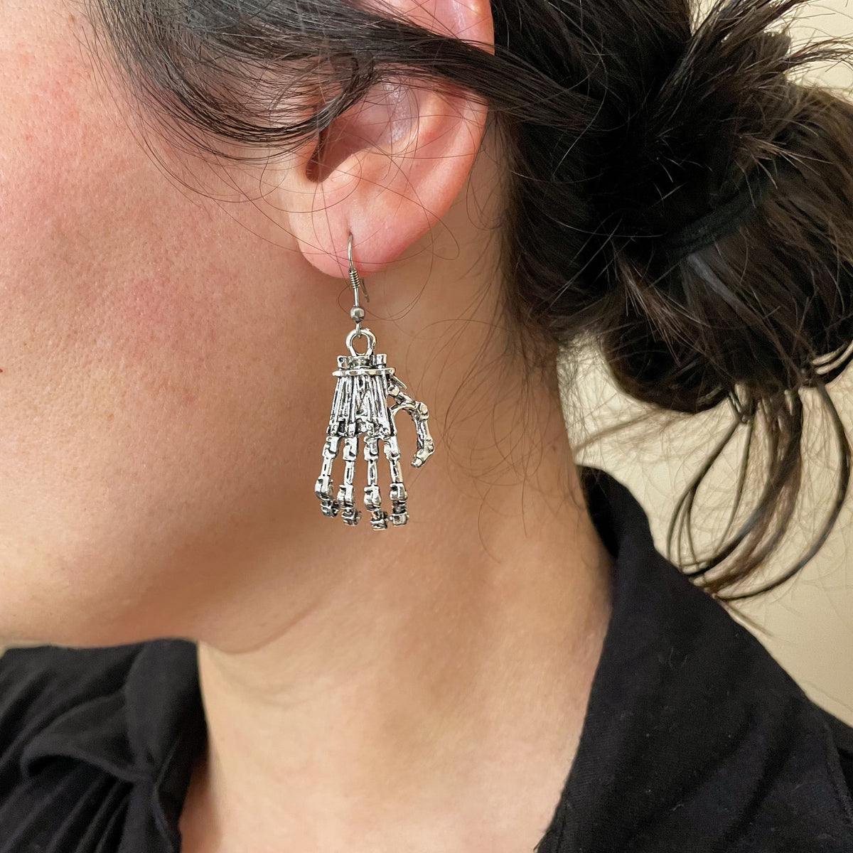 Close-up of a person wearing silver creepy hands earrings with a black top.