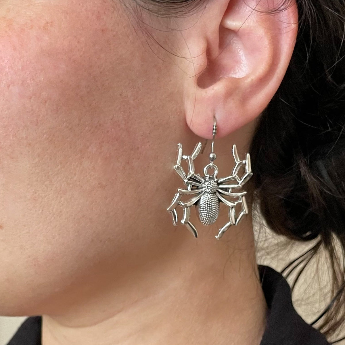 Oversized silver spider dangle earrings worn by a person